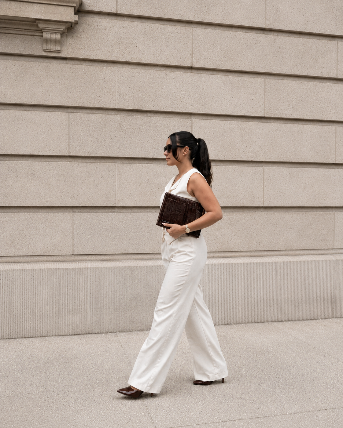 Woman in white outfit holding a brown wesbury collection macbook case against a beige wall.

